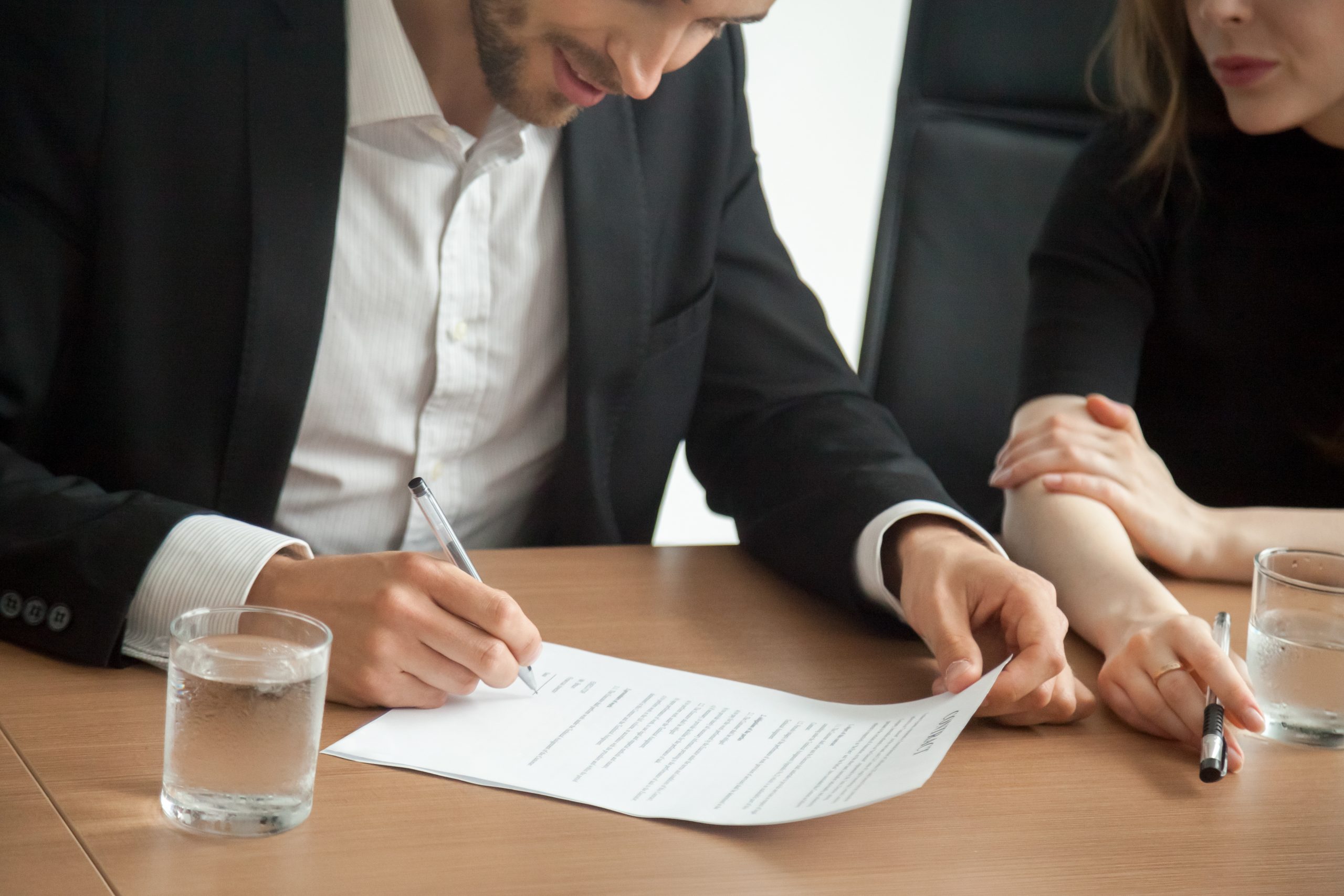 Satisfied smiling businessman in suit signing contract at meetin